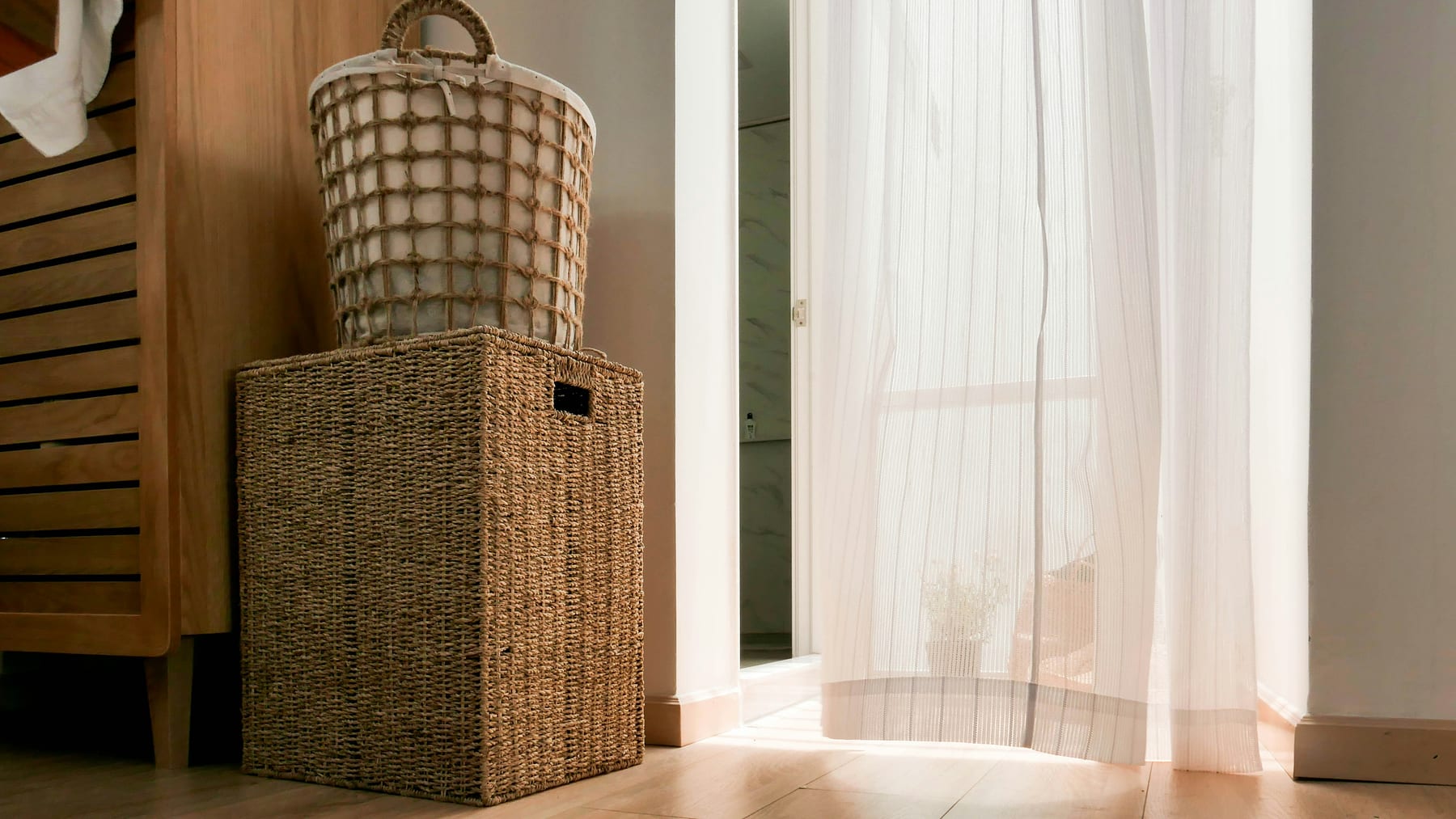 Two woven baskets by a curtained doorway, on a wooden floor in afternoon light