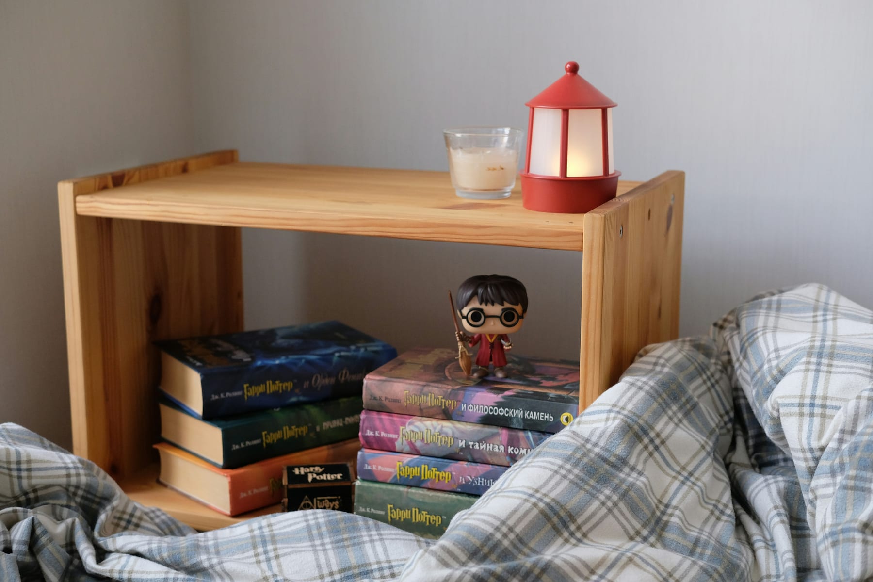 A stack of children books under a small bedside shelf, a lamp lit above them