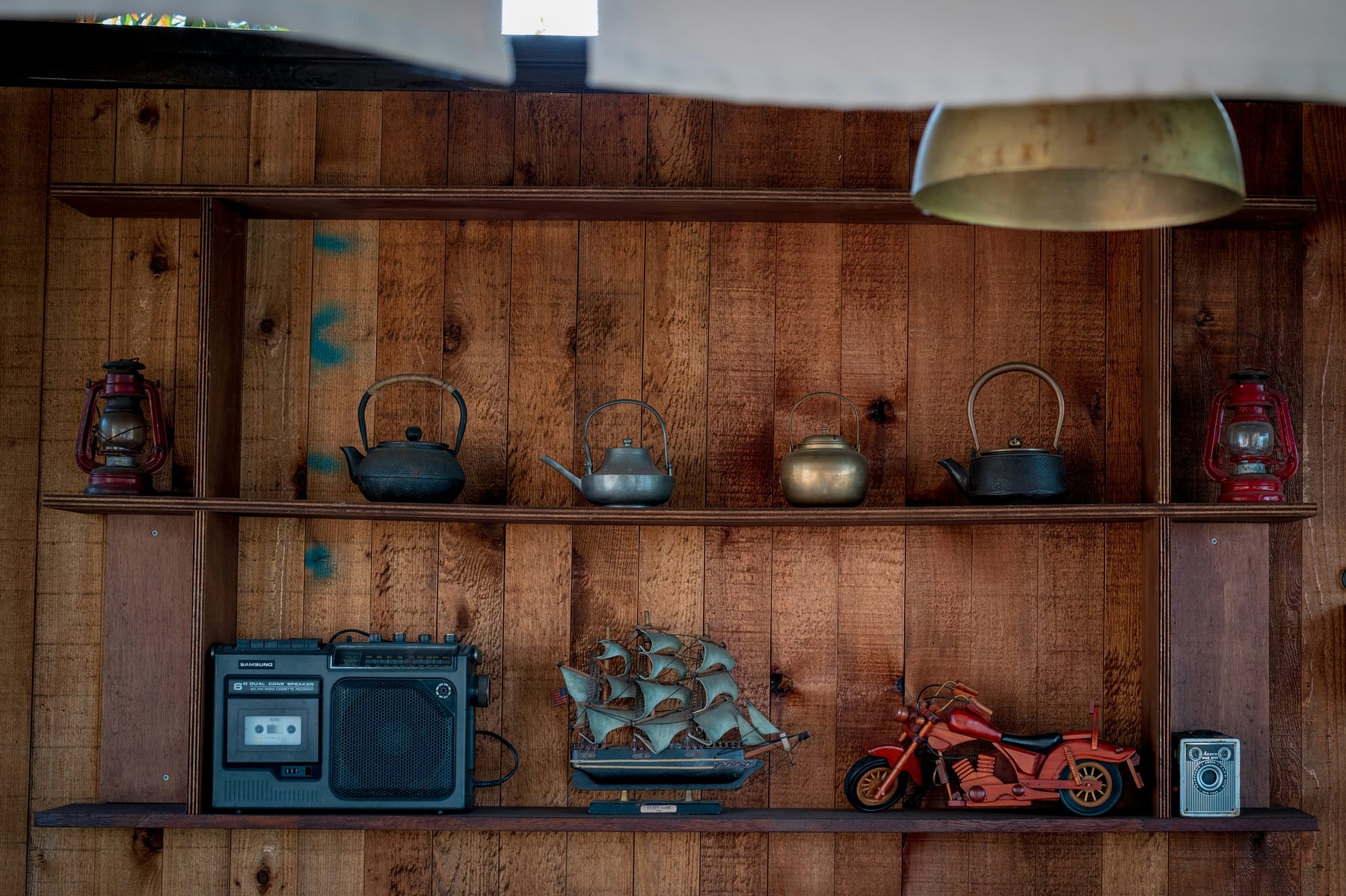 Wooden shelves on a plank wall holding kettles, lanterns and a few old objects