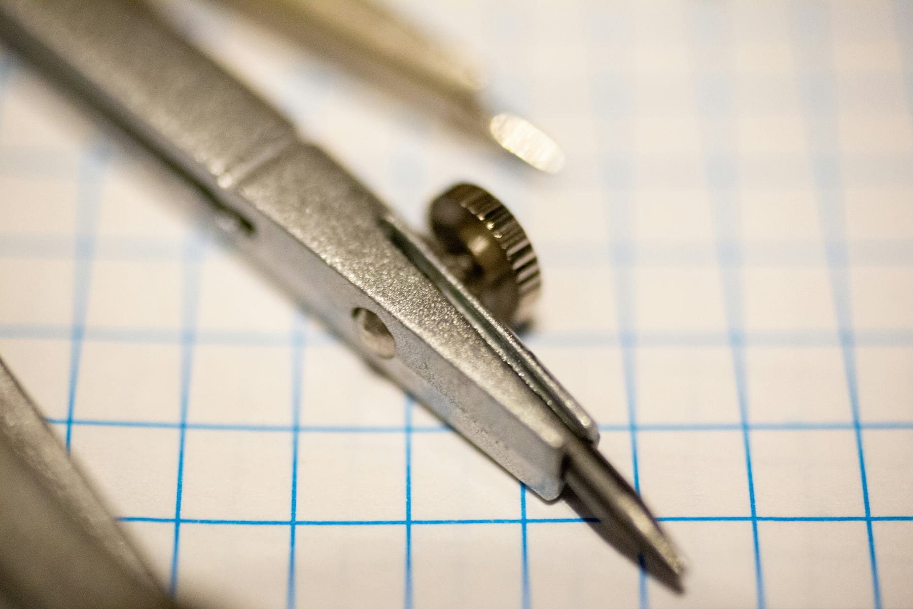 A drafting compass resting on graph paper