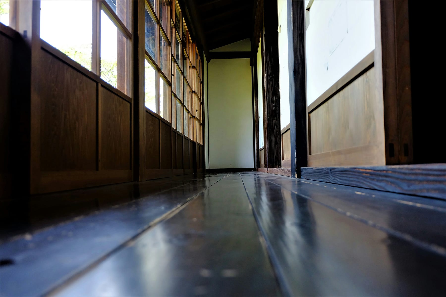 A wooden corridor running the length of a house, daylight coming through the windows along it