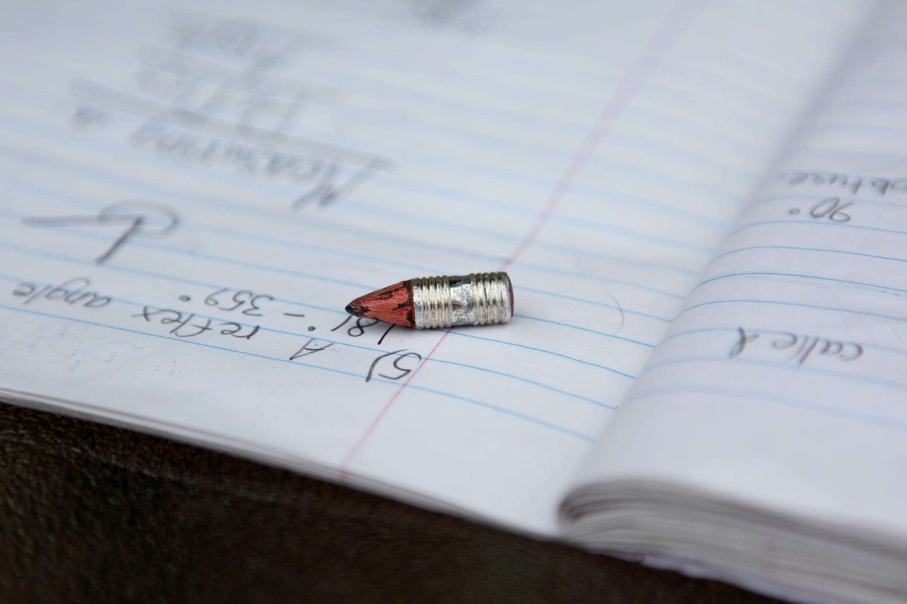 An open exercise book with a geometry problem written out in pencil, and a broken pencil tip on the page