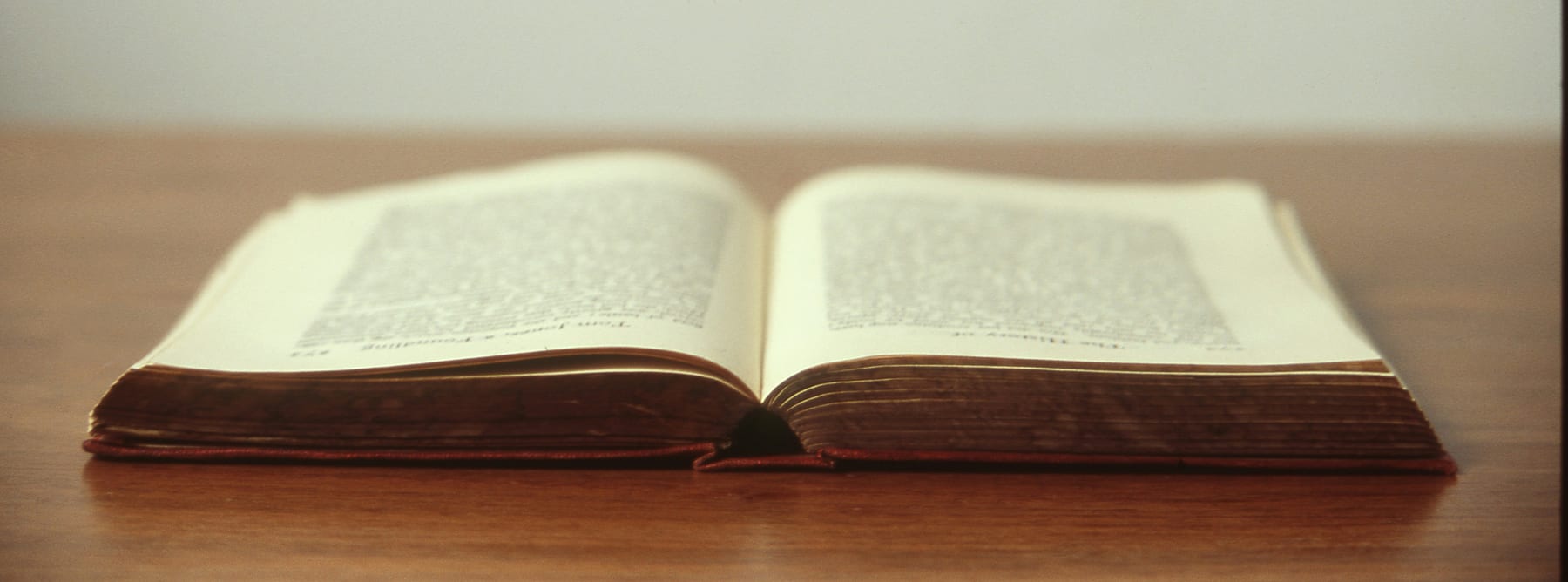 An old book lying open on a wooden table, its gilt page edges catching the light