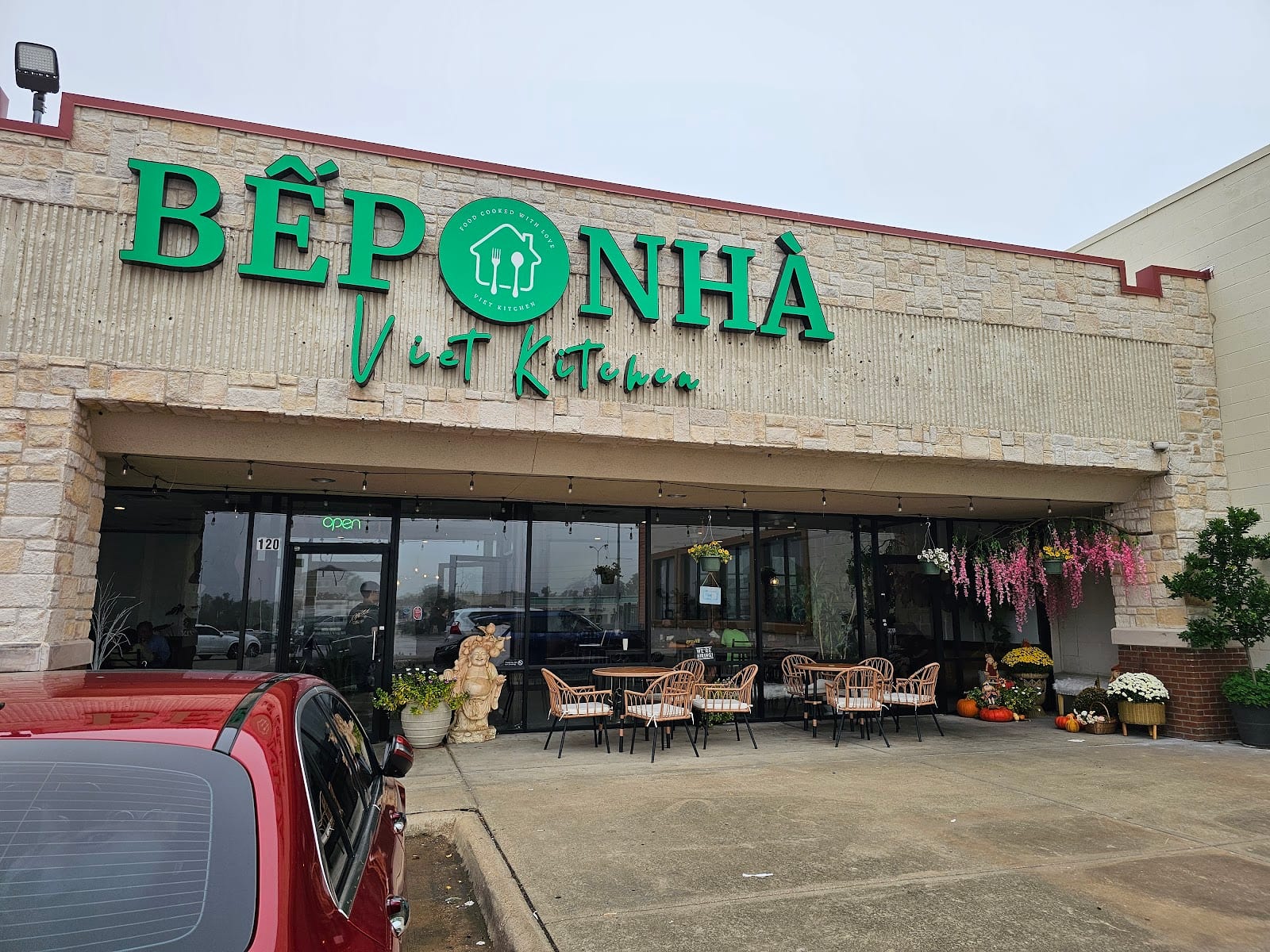 The front of Bep Nha, green lettering across the stone facade, with hanging flowers and a few patio tables under the awning.