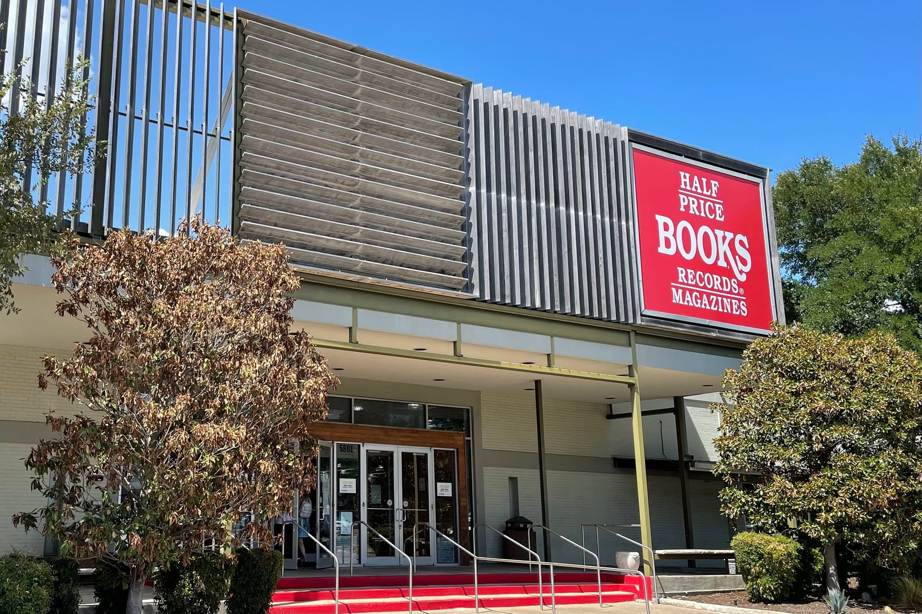 The entrance to the Half Price Books flagship on a clear day, red steps up to the doors and the big red Books Records Magazines sign above them.